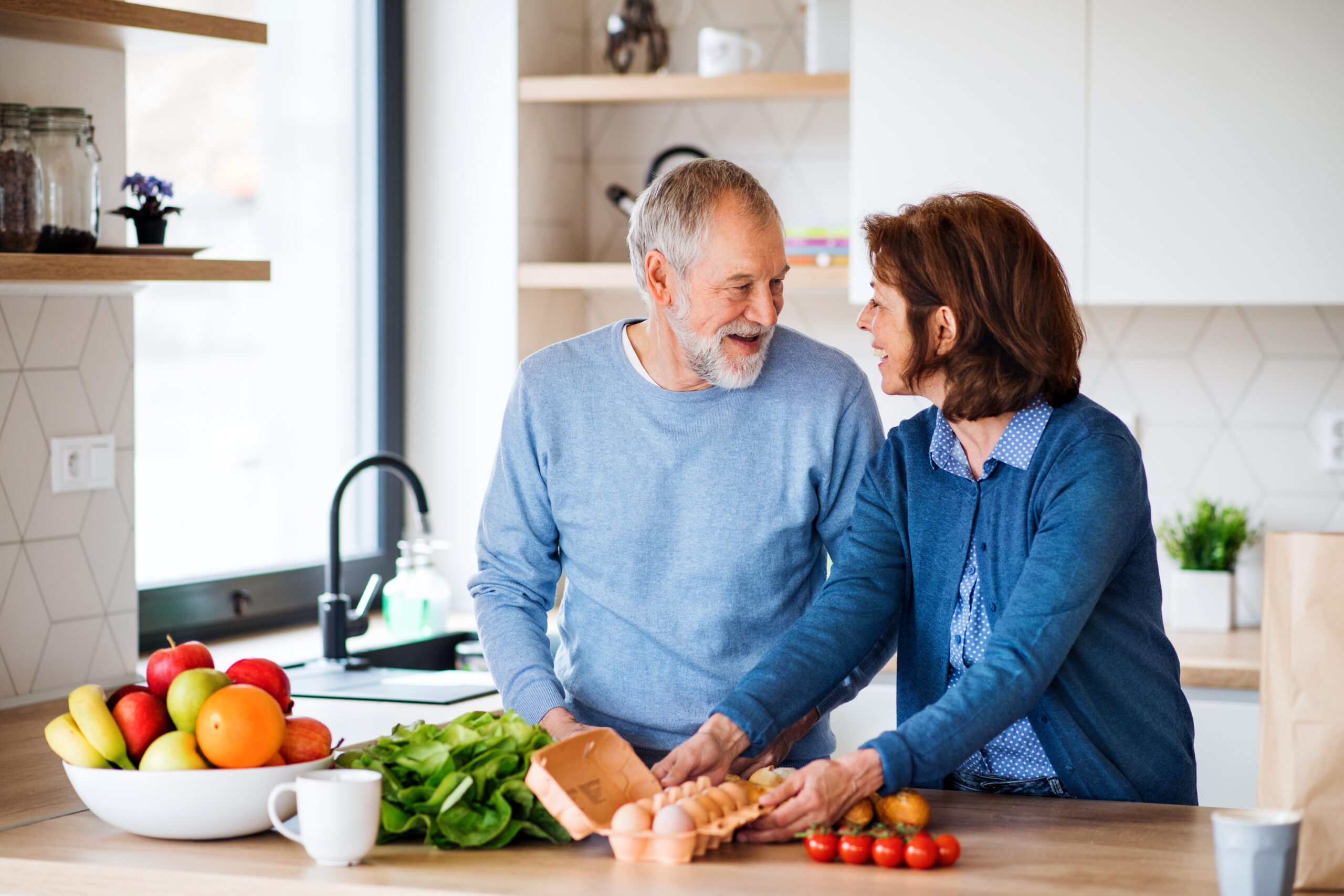 A portrait of senior couple indoors at home, unpacking shopping.